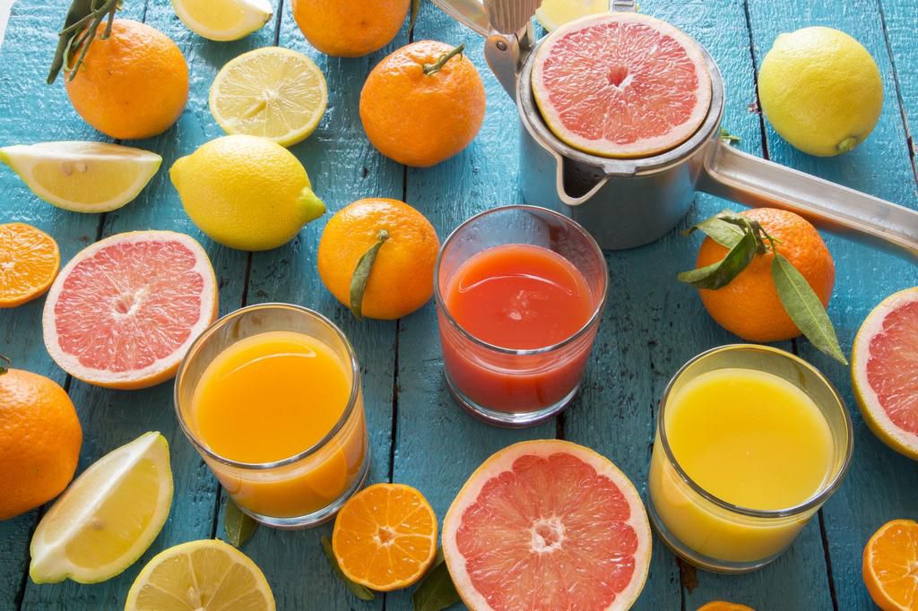 Glasses of orange juice, grapefruit juice and multivitamine juice, juice squeezer and fruits on wood