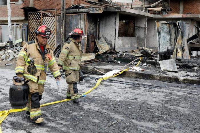Firefighters walk past destroyed houses after the explosion of a gas tanker in Lima left at least eight people dead and dozens injured