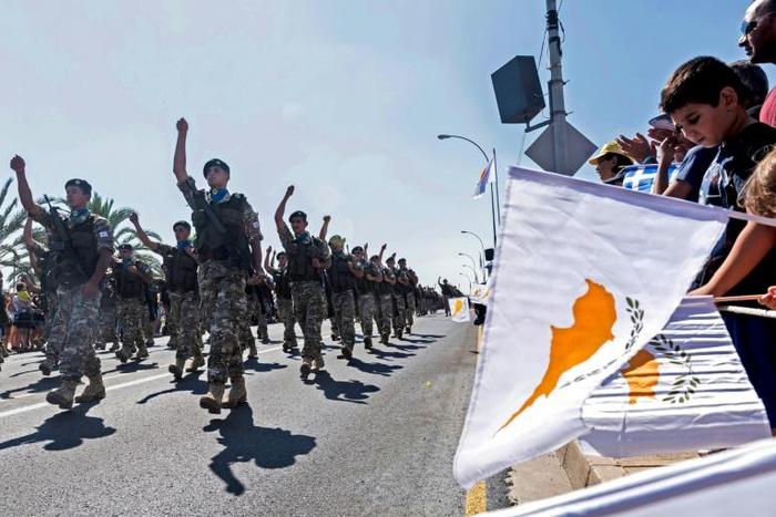 People in Nicosia wave flags during a military parade marking the 59th anniversary of Cyprus' independence from British colonial rule in October 2019