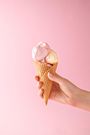 Close-Up Of Hand Holding Ice Cream Against Pink Background