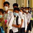 Masked Cambodian students line up to disinfect their hands with an alcohol solution before entering class at a school in Phnom Penh