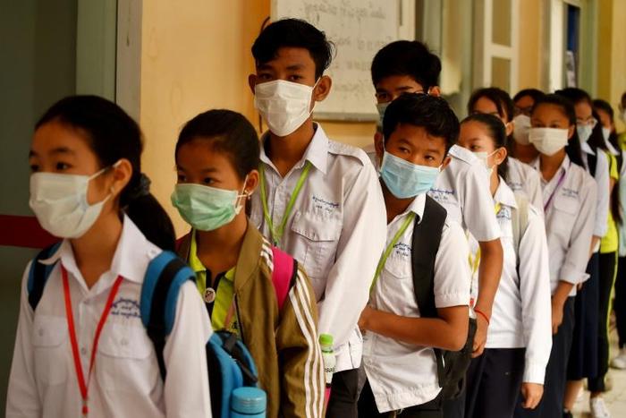 Masked Cambodian students line up to disinfect their hands with an alcohol solution before entering class at a school in Phnom Penh