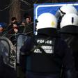 Greek riot police officers watch migrants acrss the barbed wire border