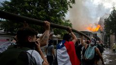 Demonstrators hold up a hose as flames engulf the Pedro de Valdivia University following a protest against the government of Chilean President Sebastian Pinera in Santiago, on November 8, 2019.Unrest began in Chile last October 18 with protests against...