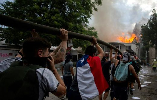 Demonstrators hold up a hose as flames engulf the Pedro de Valdivia University following a protest against the government of Chilean President Sebastian Pinera in Santiago, on November 8, 2019.Unrest began in Chile last October 18 with protests against...