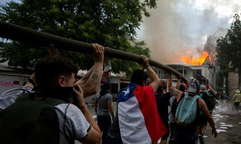 Demonstrators hold up a hose as flames engulf the Pedro de Valdivia University following a protest against the government of Chilean President Sebastian Pinera in Santiago, on November 8, 2019.Unrest began in Chile last October 18 with protests against...