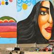 Iraqi women walk past a mural inspired by ongoing anti-government protests in Tahrir square in Baghdad while political leaders are struggling to choose a new prime minister
