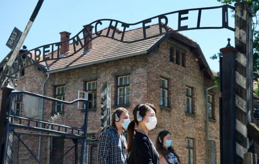 As the site reopens following Coronavirus lockdown, visitors to Auschwitz contemplate the  entrance gate with its inscription "Work sets you free"