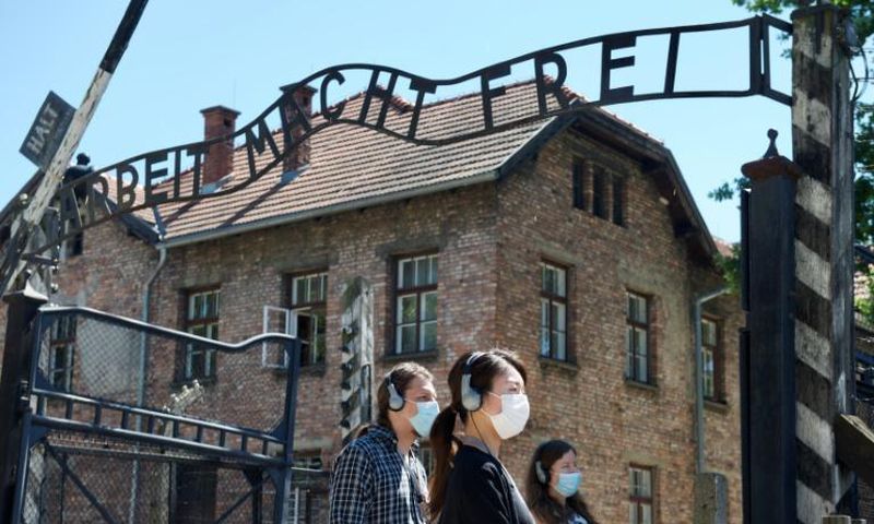 As the site reopens following Coronavirus lockdown, visitors to Auschwitz contemplate the  entrance gate with its inscription "Work sets you free"