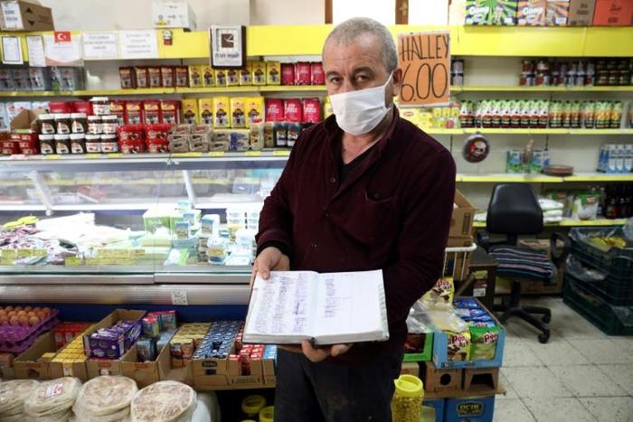 Shop owner Mudaver Uygur shows the book where he notes money owed him by costumers -- wealthier ones have stepped into the breach to pay off debts worth hundreds of dollars in some cases