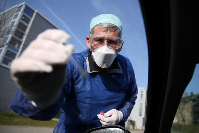 German doctor Michael Grosse takes a sample from a car driver at a drive-through testing point for the coronavirus in Halle, eastern Germany