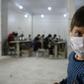A child looks on as volunteers gather in a sewing workshop to make protective face-masks in the northeastern Syrian city of Idlib
