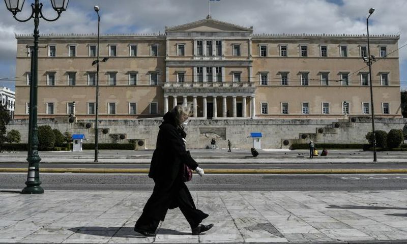 A woman wearing a face mask walks past the empty Syntagma Square in Athens, in front of the Greek Parliament early during the outbreak of COVID-91.