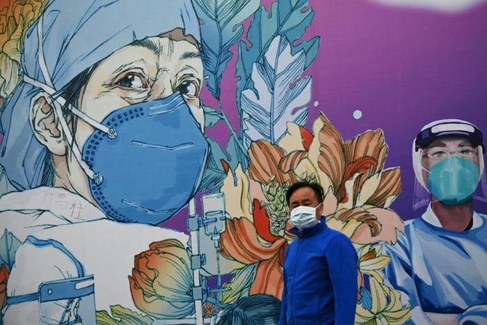 A man wearing a face mask walks past a mural at Leishenshan Hospital in Wuhan in April