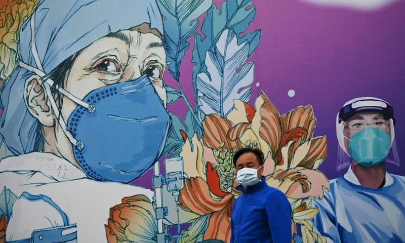 A man wearing a face mask walks past a mural at Leishenshan Hospital in Wuhan in April