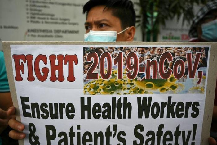 A health worker wearing a face mask holds a placard during a protest in front of a government hospital in Manila