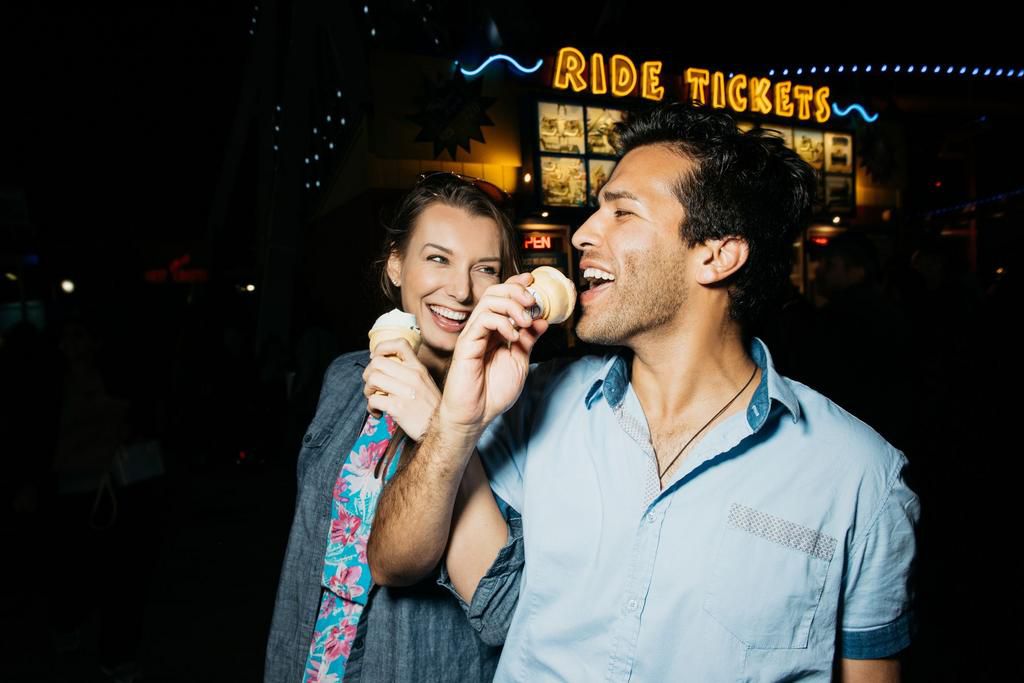 Young couple arm in arm eating ice cream in amusement park at night, Santa Monica, California, USA