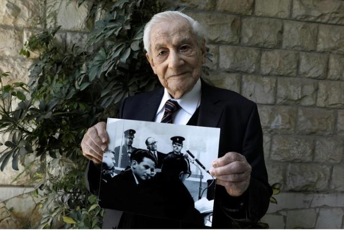 Bach, pictured holding a photograph showing himself (below) during the Eichmann trial, said, 'Not a day passes without me remembering some particular item, or some particular piece of evidence, or some particular moment from the Eichmann trial'