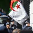 Algerian police wearing face masks stand as protesters march past during an anti-government demonstration in the capital Algiers on March 6