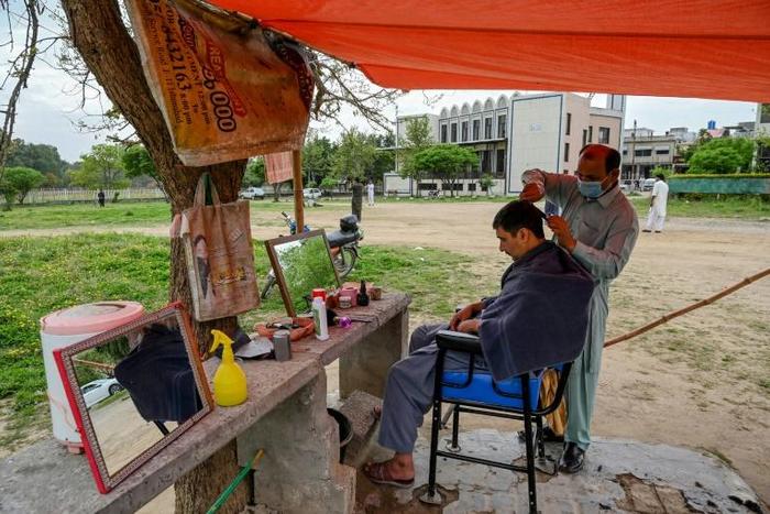 A barber wearing a facemask cuts a customer's hair at an open-air stall in Islamabad