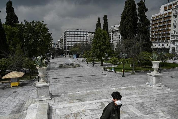 A man wearing a protective face mask walks at empty Athens' empty Syntagma square on March 23, 2020 as the country struggles to control the spread of the COVID-19, the novel coronavirus