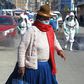 A woman dressed in typical indigenous clothing walks near municipal employees disinfecting the streets of Puno in Peru