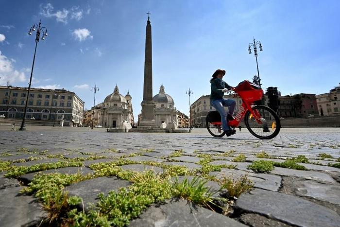 Grass grows between cobblestones as a woman rides a bicycle across Piazza del Popolo on April 24, 2020 in Rome, during the country's lockdown aimed at stopping the spread of the COVID-19 pandemic, caused by the novel coronavirus