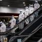 Medical staff wearing protective suits ride down an escalator at Moscow's Sheremetyevo airport