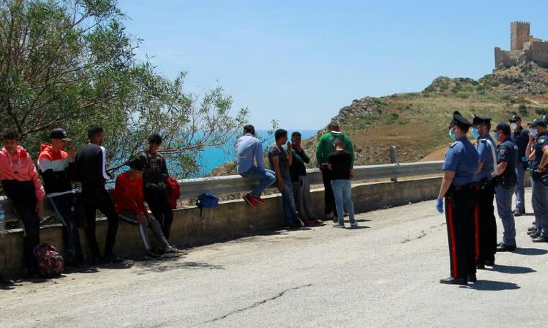 Police are shown checking and detaining some of the migrants, who left the beach in small groups