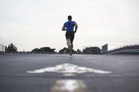 Male athlete running on a road away from camera, full length
