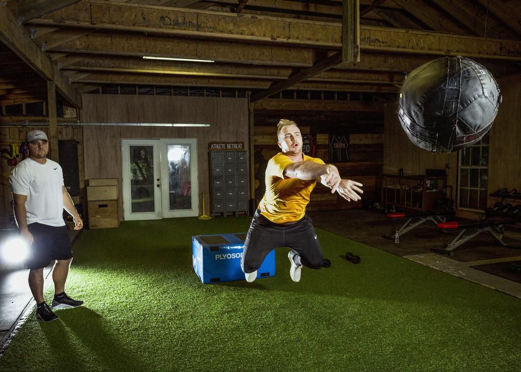 Pete Alonso, having jumped off a platform, is jumping forward and throwing a medball at the same time.