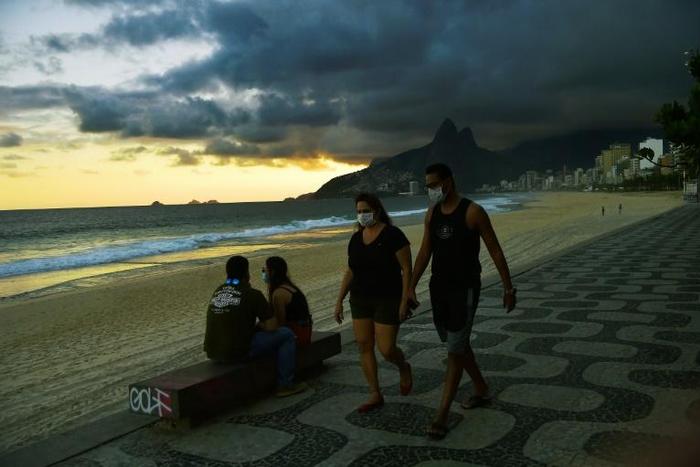 People wear face masks as they walk along Ipanema Beach in Rio de Janeiro on May 19, 2020. The peak of Brazil's outbreak is not expected until June