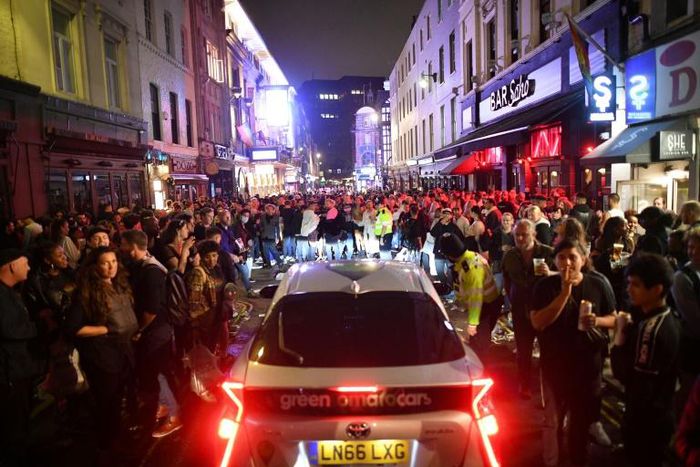 A car tries to drive along a street filled with people drinking in the Soho area of London