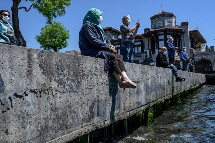 People over 65 wearing protective face masks sit and enjoy the sun on the Bosphorus in their first trip outdoors since a tough coronavirus lockdown was imposed nearly two months ago