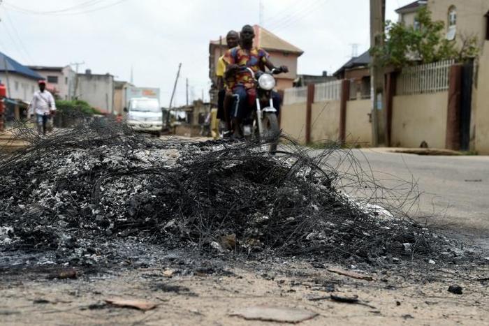 A motorcycle taxi in the district of Ojodu drives past the remains of a fire set to ward off gangs of robbers