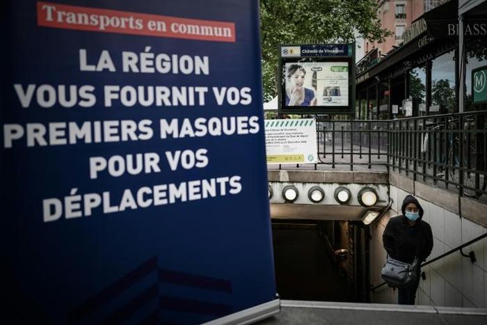 A woman wearing a protective mask walks out of a metro station next to a sign announcing the distribution of face masks to commuters after complaints over shortages of supplies to medical professionals