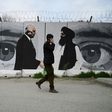 A man wearing a facemask walks past a mural in Kabul depicting the troop withdrawal agreement signed by US Special Representative Zalmay Khalilzad and Taliban co-founder Mullah Abdul Ghani Baradar