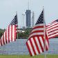 A SpaceX Falcon 9 rocket with the Crew Dragon spacecraft looms in the distance at launch complex 39A as American flags flutter in the wind, at the Kennedy Space Center in Florida on May 29