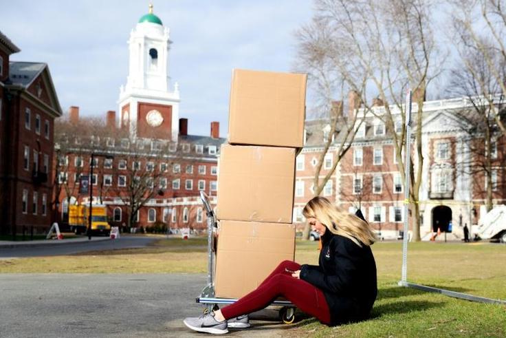 A Harvard student sits with her belongings before returning home on March 12, 2020, as students left campus due to the coronavirus pandemic