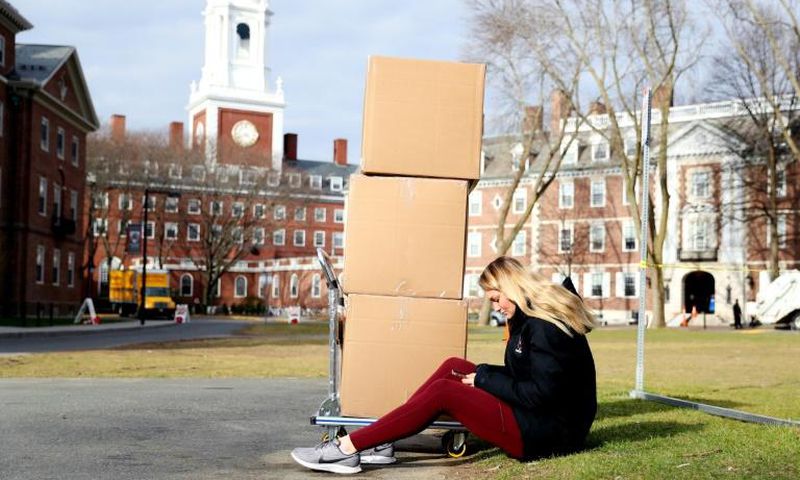 A Harvard student sits with her belongings before returning home on March 12, 2020, as students left campus due to the coronavirus pandemic