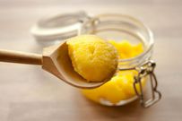 Ghee clarified butter desi in glass jar with spoon made from wood on natural wooden background