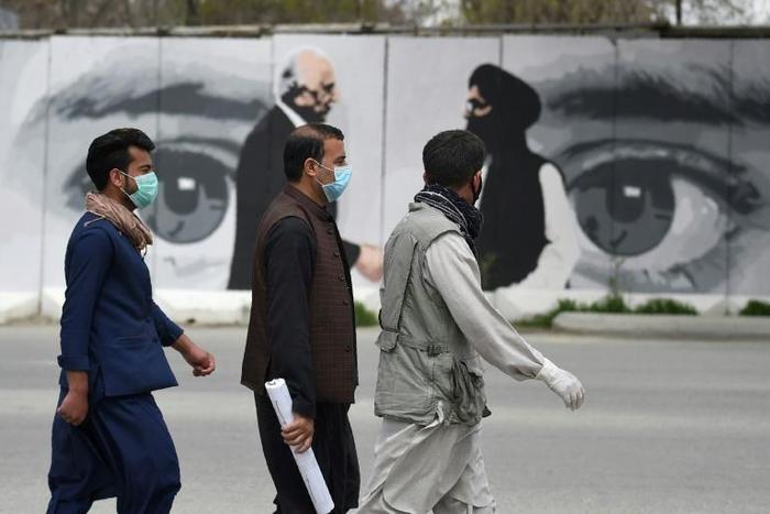 A man wearing a facemask against coronavirus walks past a wall painted with images of US Special Representative for Afghanistan Reconciliation Zalmay Khalilzad and Taliban co-founder Mullah Abdul Ghani Baradar, in Kabul