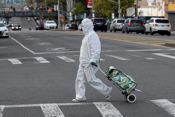 A woman wearing a hazmat suit and googles pulls her grocery cart through New York City on April 20, 2020