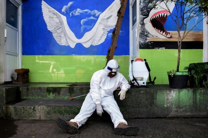 An Indonesian health agency official rests at the entrance to a public toilet as other colleagues conduct COVID-19 testing in Bandung, West Java