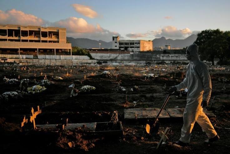 A funeral worker wearing protective clothing as a preventive measure against the coronavirus walks through Caju Cemetary in Rio de Janeiro on May 9