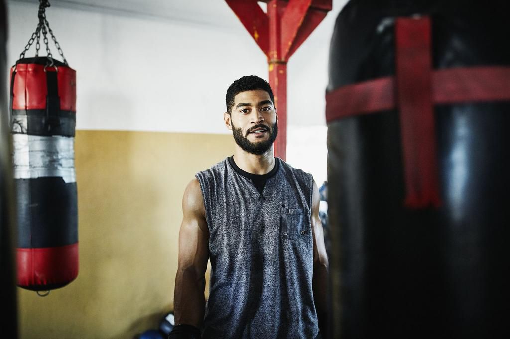 Portrait of male boxer standing by heavy bag in boxing gym