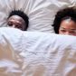 African couple peeking over their bedsheets while lying together in their bed
