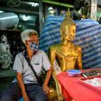 A vendor wearing a face mask against the spread of the coronavirus sits beside a Buddha statue as he waits for customers at an amulet market in Bangkok