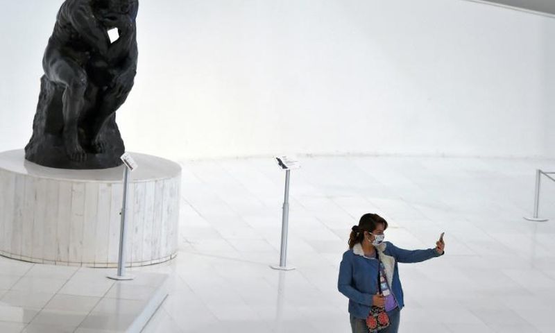 A visitor -- wearing a face mask -- takes a selfie at the Soumaya Museum in Mexico City in front of a Rodin sculpture