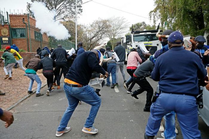 Protesters run from a stun grenade fired by police outside the Zimbabwean Embassy in South Africa's Pretoria